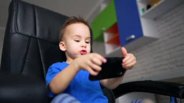 Sevimli iki yaşındaki çocuk akıllı telefona dikkatle bakıyor. Bilgisayar oyunu oynayan küçük bir çocuk. Düşük açı görünümü.
