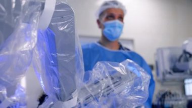 Plastik kaplı robot kol hareket halinde. Kapatın. Erkek doktor arka planda kontrolü elinde tutuyor.