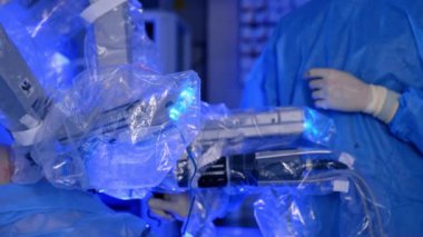 Hastayı ameliyat eden teknolojik robot cerrah. Plastikle kaplı manipülatör kollar yavaşça laparoskopik ameliyat yapıyor. Tanımlanamayan doktor arka planda kırpılmış resim.