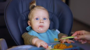 Sevimli beyaz bebek annesinin elinden kaşığı alıyor. Küçük çocuk kaşığı ağzına dayıyor. Kapat..