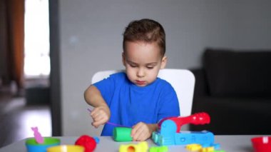 Masada oturan küçük konsantre çocuk plastikinle oynuyor. Şirin çocuk büyük bir parça kumaşı kesmek için sopa kullanıyor..