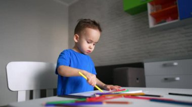 İki yaşındaki erkek bebek uzun sarı bir kalemle çiziyor ve seçiyor. Küçük çocuk evde sanat etkinliği yapıyor. Düşük açı görünümü.