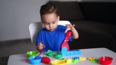 Çekici beyaz çocuk plasticinle oynuyordu. Küçük çocuk plastikçiyi sıkıştırmak için özel bir makine kullanıyor..