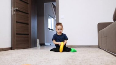 Oyuncak piramidin detaylarıyla oynayan iki yaşında bir çocuk. Çocuk halıya oturup oyuncağı yere yuvarlıyor..