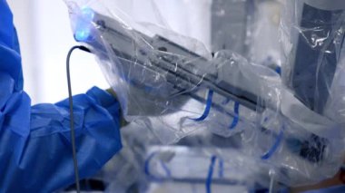 Robot cerrah kolu insan doktorun koluyla birlikte çalışıyor. Erkek doktor çalışırken laparoskopik araçlar kullanır.