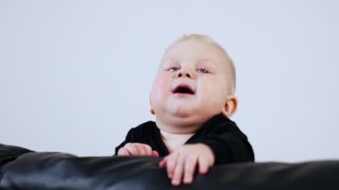 Siyah süveterli, deri koltukta gülümseyen tombul bir bebek. Beyaz arka planda sevimli çocuk portresi.