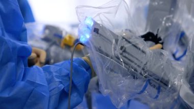 Robot cerrahın kolunu oynatmak. Doktorun eli mavi bornozda laparoskopik alet cihazını tutuyor..