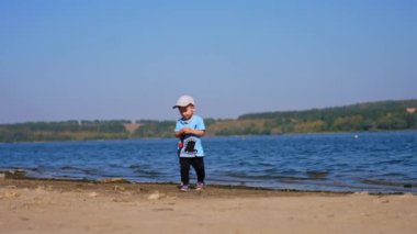 Tatlı çocuk kumlu nehir kıyısında etrafta başka kimse olmadan yürüyor. Bebek bir taş aldı ve onu suya attı..