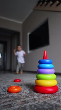 Bebek çocuk oyuncak piramidinin yanındaki odaya koşuyor. Sevimli çocuk oyuncağı monte etmeye başlıyor. Dikey video.