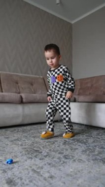 Kareli pijama giyip oyuncak toplayan iki yaşında bir çocuk. Bebek çocuk bir oyundan sonra oyuncakları toplar. Dikey video.