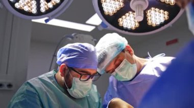 İki işbirlikçi cerrah travma cerrahisinde büyük yuvarlak lambaların altında çalışıyor. Doktorlar modern operasyon odasında işlem yapıyorlar..