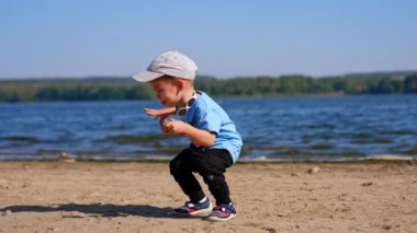 Kafkasyalı çocuk kumlu sahilden taş topluyor. Tatlı çocuk kayayı suya atıyor ama kıyıya düşüyor..