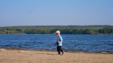 Yazın nehir kıyısında yürüyen küçük bir çocuk. Küçük çocuk yerden bir taş aldı ve atmak için suya koştu..
