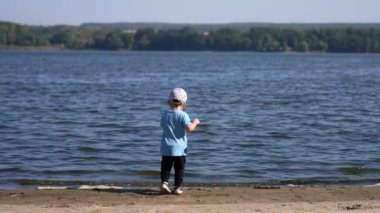 Enerjik erkek çocuk nehre koşar ve bir taş atar. Yürüyen çocuk döndü ve kumsalda yürürken kameraya yaklaştı..