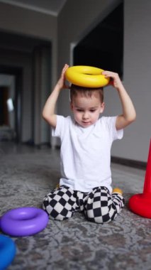 Koyu saçlı erkek bebek oyuncak piramidi kafasına takıyor. Bir oyuncak yere düşer ve çocuk sevinçle alkışlar..