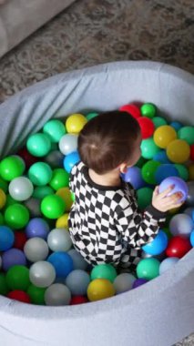 Siyah beyaz pijamalı bebek kuru havuzda oturuyor. Gülümseyen oyuncu çocuk havuza top atar ve yuvarlanır..