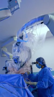 Doktor ileri düzey tıbbi mikroskobun arkasında nöroşirürji yapıyor. Kadın doktor da yardım ediyor ve mikroskoba bakıyor. Dikey video.