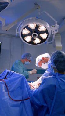 Nöroşirürji ameliyatı yapan iki doktorun yardımıyla erkek beyin cerrahı. Ana cerrah parlak yuvarlak lambanın altında çalışır. Dikey video.