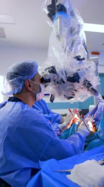 Profesyonel beyin cerrahı mikroskoba bakar ve cerrahi aletler kullanır. Mikro cerrahi yapan bir doktorun yan görüntüsü. Dikey video.