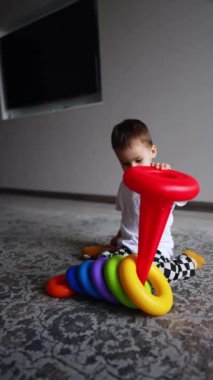 Küçük çocuk piramidi kırıyor. Çocuk oyuncak temelini odasında yerde oturarak tutuyor. Mutlu çocuk oyun zamanı.