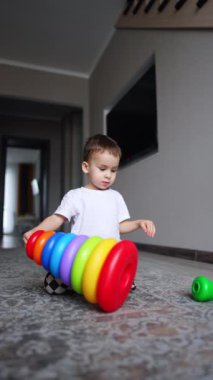 Yerde oturan tatlı çocuk piramidi baş aşağı çeviriyor. Çocuk oyuncağı söküp yeniden yapmaya başlıyor. Düşük açı görünümü.