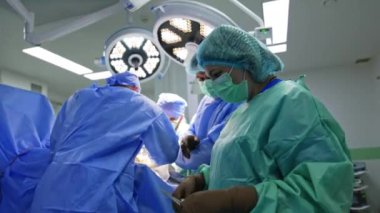 Koruyucu üniforma giyen ve maske takan kadın bir ameliyat hemşiresi baş cerrahlara aletleri verir. Modern operasyon odasında travma cerrahisi gelişimi.