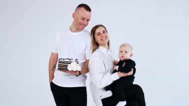 Küçük bebeklerinin 8 ayını kutlayan üç kişilik mutlu bir beyaz aile. Stüdyoda anne, baba ve oğlunun portresi. Beyaz arkaplan.