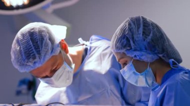Kadın ve erkek cerrahlar ameliyatta maske, kep ve bornoz takıyor. Odaklanmış doktorlar sinir cerrahisi yapıyorlar..