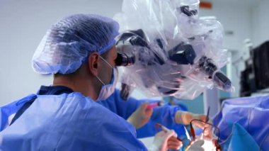 Beyin cerrahı elektrikli aletleri uyguluyor ve mikroskoba bakıyor. Asistan aletleri hemen doktora verir..