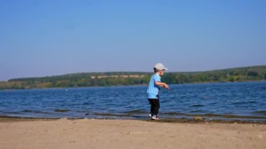 Küçük çocuk taşları nehre atıyor. Bebek yazın güneşli sahilde yürüyor..
