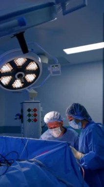 Operasyon masasında işbirliği yapan iki doktor. Erkek ve kadın cerrahlar yuvarlak lambanın altında ameliyat yaparlar. Dikey video.