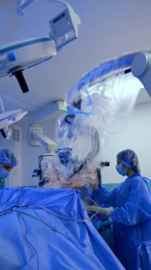 Ameliyat masasının üstünde cerrahi mikroskop var. Cerrah mikroskobun arkasında oturur ve yardımcı doktor yanında durur. Dikey video.