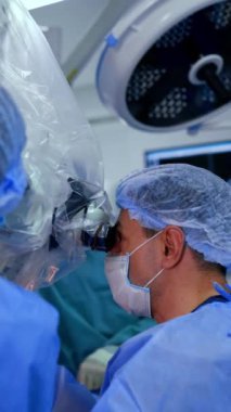 Mikroskop dürbünlerine bakan bir erkek doktorun üst kısmı. Beyin cerrahisi devam ediyor. Dikey video.