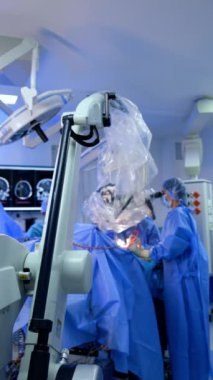 Gelişmiş mikroskop çalışma masasının üstündedir. Ameliyathanede hastayı iki doktor ameliyat ediyor. Dikey video.