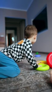 Aktif enerjik bebek evde oyuncaklarıyla oynuyor. Çocuk pantolonunu yukarı çekti ve oyuncakları odaya fırlattı. Dikey video.