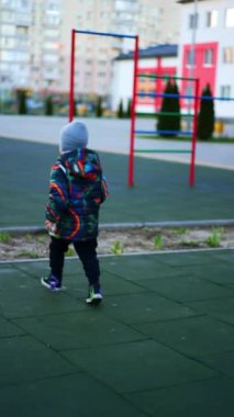 Çocuk parkında koşan ceketli küçük çocuğu takip ediyorum. Aktif enerjik bebek dışarıda eğleniyor. Dikey video.