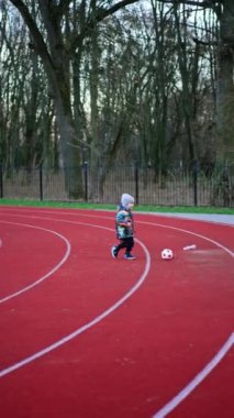 Hoş çocuk topu takip ederek stadyumun yanından geçiyor. Sonbaharda dışarıda futbol oynayan mutlu, aktif bir çocuk. Dikey video.