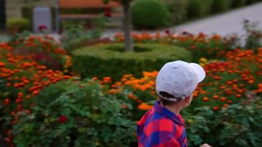 Kareli tişörtlü ve şapkalı gülümseyen bebek çiçek tarhında koşuyor. Mutlu çocuk onu alan dedesinin yanına koşar. Büyükbaba ve torun parkta..