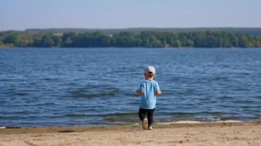 Küçük çocuk nehre gelip biraz kum atıyor. Bebek yazın nehir kıyısında eğleniyor..