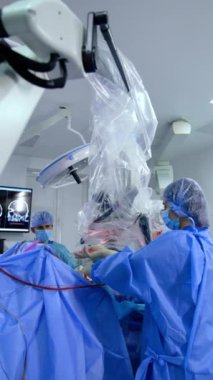 Kadın asistan ameliyat sırasında şırıngayı erkek doktora veriyor. Erkek ameliyathane hemşiresi, metal aletleri doktorun dürbüne bakması için verir. Dikey video.