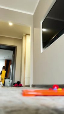 Sağlıklı, aktif, beyaz bir erkek bebek kameradan kaçıyor. Küçük çocuk odanın önünden geçti ve tekrar kameraya yaklaştı. Düşük açı. Dikey video.