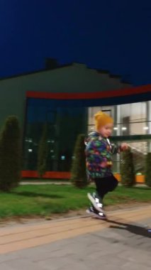 Enerjik küçük çocuk dışarıda mutlu bir şekilde koşuyor. Aktif çocuk akşamları sabun köpüğü yakalıyor ve zevk alıyor. Düşük açı. Dikey video.