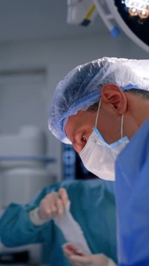 Kafkas cerrahı hastaya odaklanmış görünüyor. Doktora yardım etmek arka planda bandajları hazırlar. Dikey video.