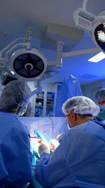 Nöroşirürji ameliyatındaki iş birlikçi meslektaşların arka görüşü. Modern ameliyathanede iki doktor ameliyat yapıyor. Dikey video.