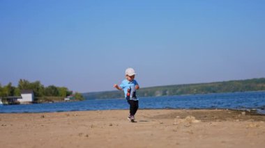 Nehir kıyısında neşeli bir şekilde koşan tatlı bir erkek bebek. Çocuk taşı alır ve suya atmak için taşır..