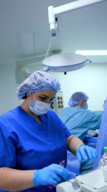 Üniformalı kadın hemşire ameliyathanede çalışıyor. Mavi üniformalı sıhhiye, infüzyon pompası makinesinin ilaçlarını hissediyor. Dikey video.