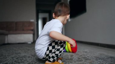 Küçük çocuk renkli bir piramide doğru koşuyor. Mutlu küçük çocuk evde neşeyle oynuyor..