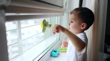 Pencere camına yapışmış bir oyuncakla şirin beyaz bir bebek oynuyor. Küçük çocuk oynar ve pencereye bakar..