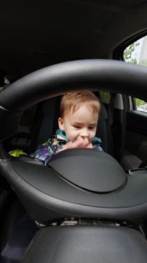 Arabada şoför koltuğunda oturan küçük, beyaz bir bebek. Bebek çocuk arabanın panellerini paçavrayla temizliyor..