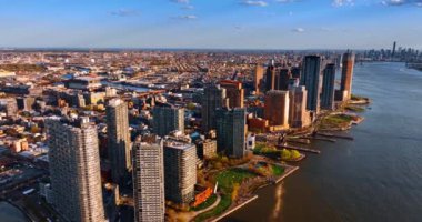 Long Island, New York 'taki East River' ın rıhtımındaki güzel binalara daha yakın uçuyor. Geniş şehir manzarası batan güneşle aydınlanır.